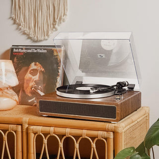Bluetooth record player with wooden finish on wicker table, vinyl and decor in cozy room