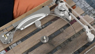 Clear turntable with silver tonearm and belt drive on wooden outdoor table