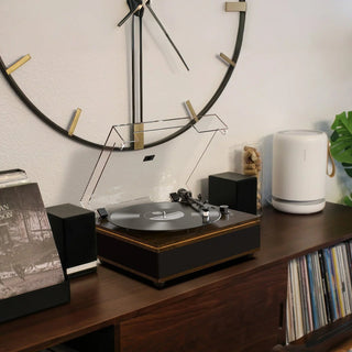 Bluetooth turntable with built-in speakers on wooden shelf, large wall clock behind