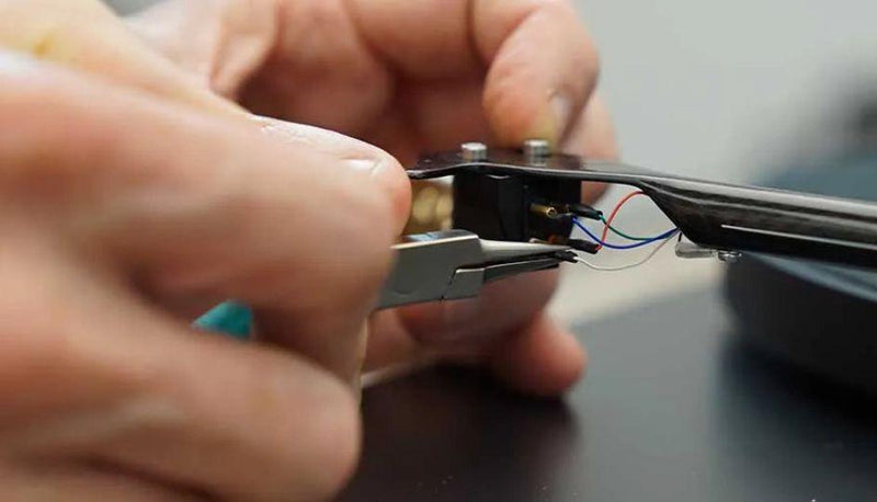 Close-up of hands replacing turntable cartridge with pliers and connecting wires