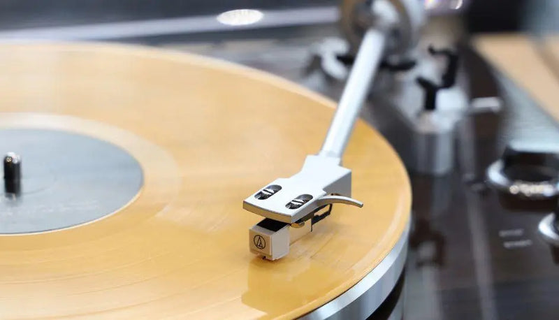 Close-up of a turntable tonearm playing a yellow vinyl record