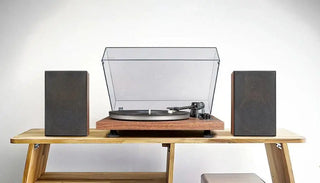 Turntable with dust cover and two speakers on wooden table, minimalist audio setup