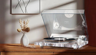 Modern clear turntable with vinyl record on wooden table, vase with dried flowers beside