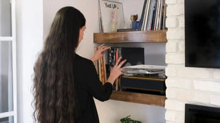 Woman selecting vinyl records near a modern record player with built-in speakers on shelf