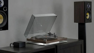 Modern vinyl record player with dust cover on wooden cabinet, flanked by speakers