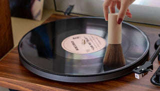 Hand cleaning vinyl record on turntable with soft brush, record player maintenance