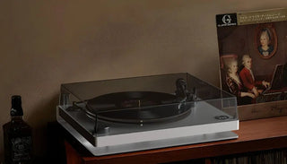Modern turntable playing vinyl record with whiskey bottle and classical music album nearby