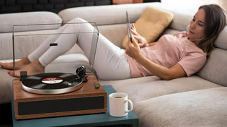 Woman relaxing on sofa with tablet near high-fidelity record player and coffee mug