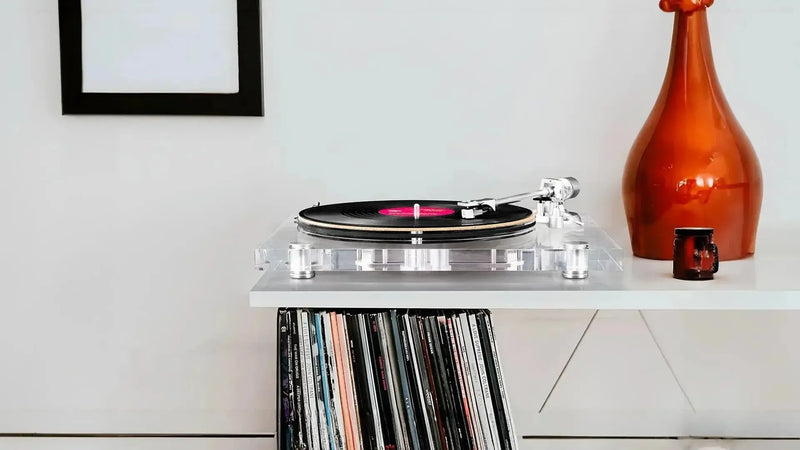 Modern turntable with vinyl record on white shelf, vinyl records below, orange vase decor