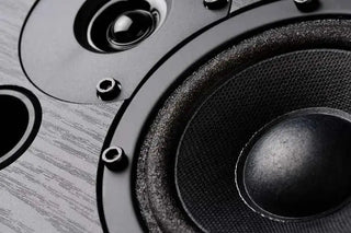 Close-up of a black audio speaker and woofer on a wood grain surface