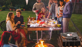 Group enjoying outdoor dinner with vintage record player on table, string lights and fire pit